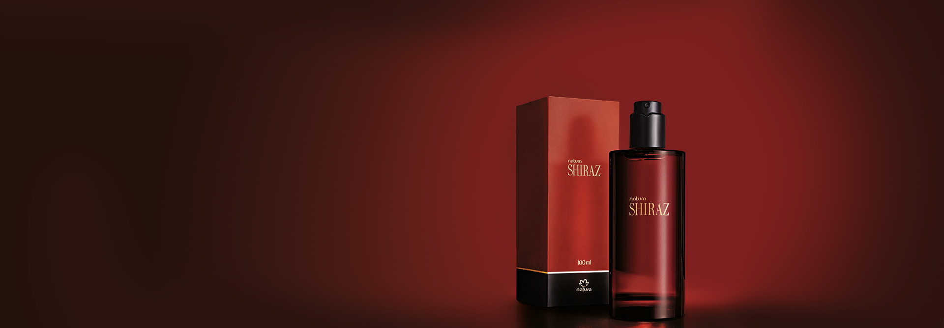Desodorante Colônia Natura Shiraz sobre fundo degradê vermelho. O frasco e a caixa são vermelhos com detalhes em preto e dourado. 