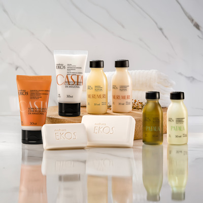 Kit de amenidades Natura Ekos com sabonetes, cremes e óleos das linhas Castanha, Murumuru e Patauá, organizados sobre base de madeira com toalhas e flores secas ao fundo.