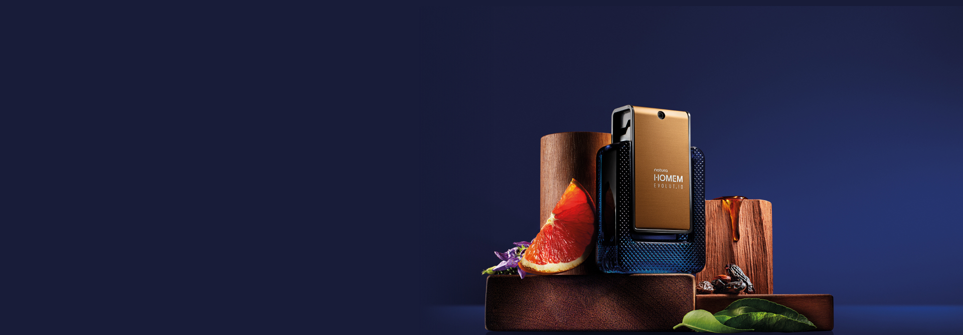 Deo Parfum Natura Homem Evolut.io sobre bloco de madeira em fundo azul. A embalagem azul e dourada está rodeada de frutos, flores, madeiras e folhas dos ingredientes da fragrância.