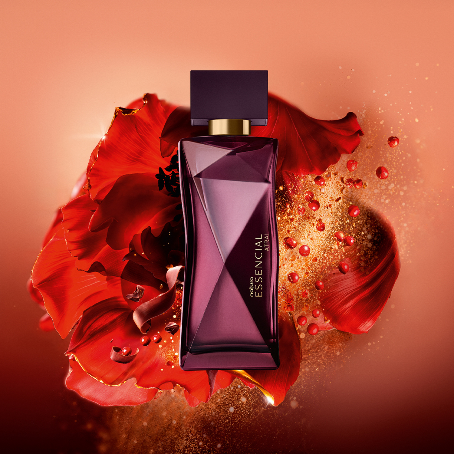 Frasco Deo Parfum Essencial Atrai Feminino em tons de vinho e dourado em destaque sobre flores vermelhas, raspas de chocolate e pimenta rosa, elementos que remetem aos ingredientes. Fundo alaranjado. 