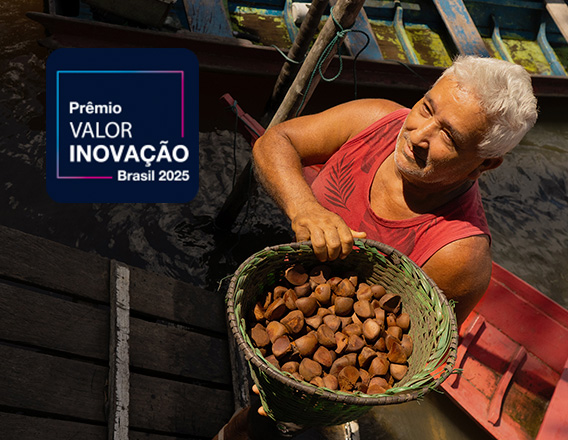 Um homem mais velho com cabelo grisalho está em um barco e carrega uma cesta cheia de castanhas do Brasil. No canto superior esquerdo, há um logotipo que diz "Prêmio VALOR INOVAÇÃO Brasil 2025".