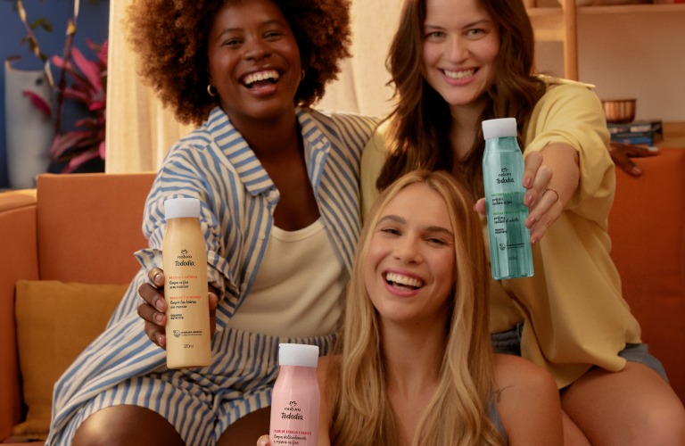 3 mulheres segurando produtos para tratar o cabelo ressecado. Elas estão felizes e sentadas em um sofá