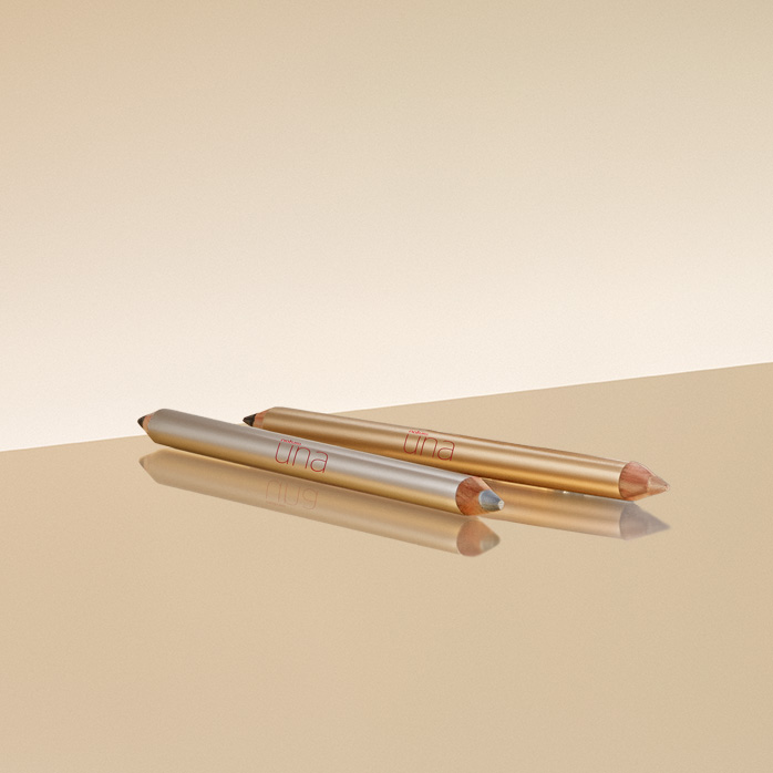 Dois tons de Lápis Natura Una Celebrar, prateado à esquerda e dourado à direita sobre bancada e fundo em amarelo-claro.