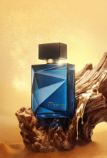 Frasco de Essencial Oud Masculino, em tom de azul-escuro e tampa preta, aparece iluminado em superfície e fundo dourados.