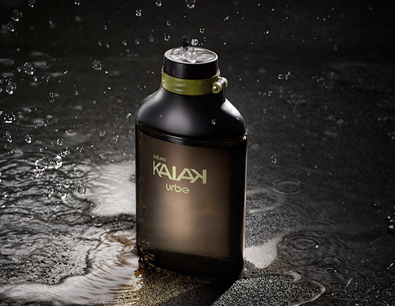 Frasco preto e verde fosco de fragrância Desodorante Colônia Kaiak Urbe sobre superfície molhada com respingos e gotas em fundo escuro.