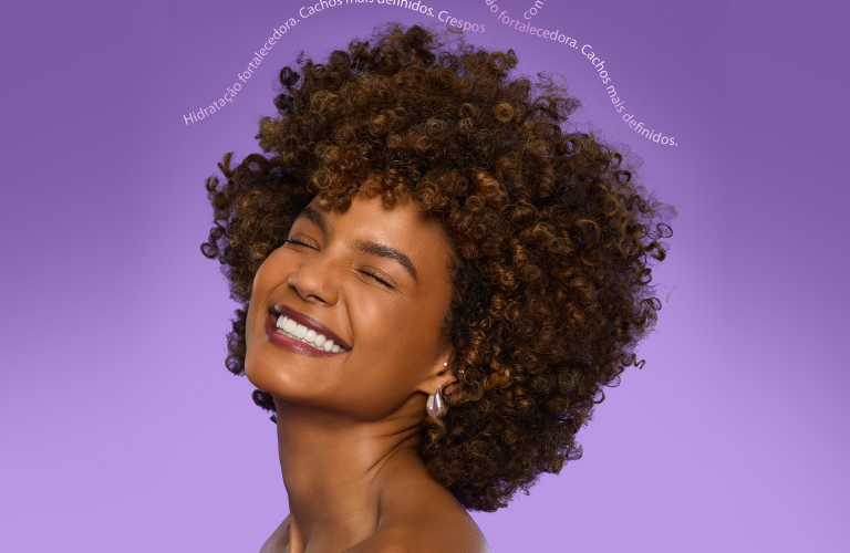 Mulher sorrindo depois de usar óleo de coco no cabelo. Seus fios estão com cachos definidos e hidratados