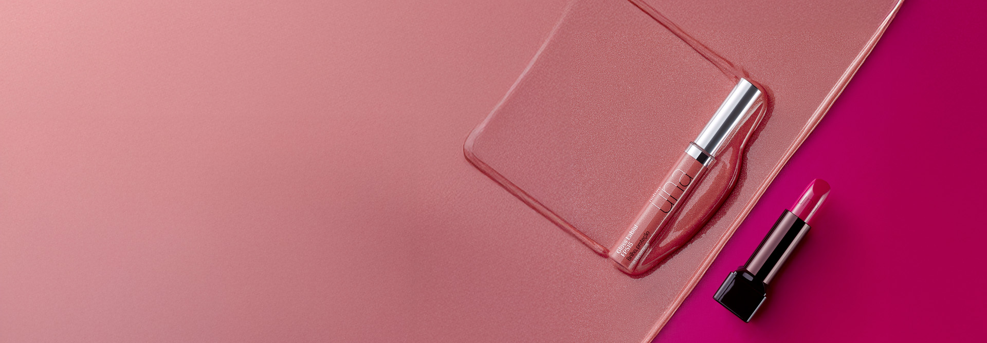 Embalagem de Gloss Labial Natura Una com tampa prata sobre textura cintilante em tom rosado. Em diagonal, à direita, embalagem preta com bala rosa de Batom Natura Una sobre fundo rosa.