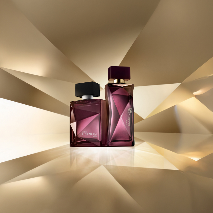 Essencial Atrai Feminino e Masculino, com frascos em tons de roxo e tampa preta, aparecem em destaque sobre fundo dourado multifacetado, que faz alusão ao design dos frascos de Essencial.