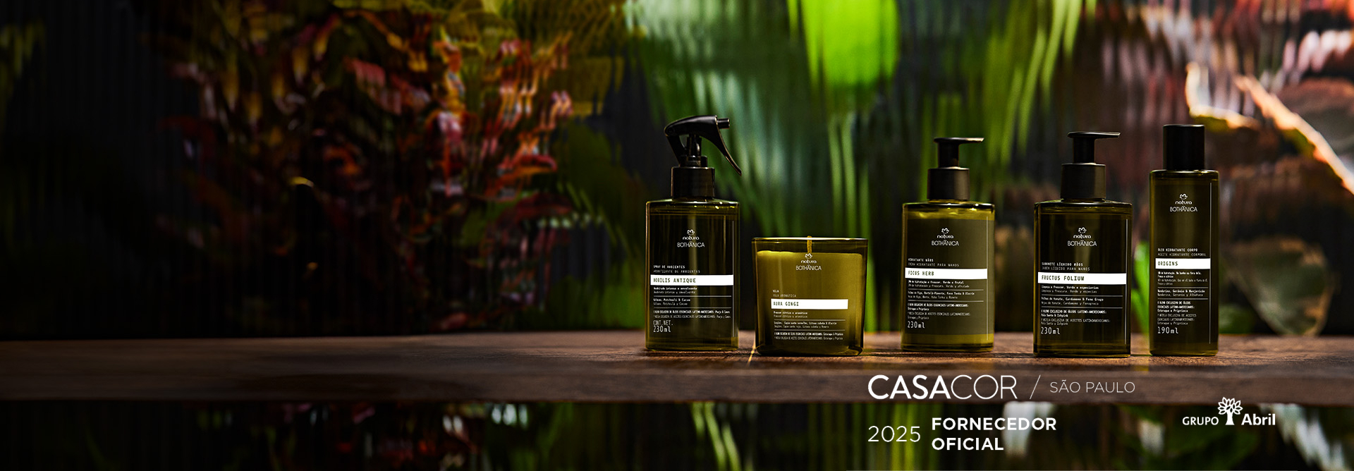 Produtos Natura Bothânica, com frascos verde-escuros sobre superfície de madeira com vidro texturizado e folhagens coloridas ao fundo. Ao lado, selo "Fornecedor Oficial Casacor São Paulo 2025".
