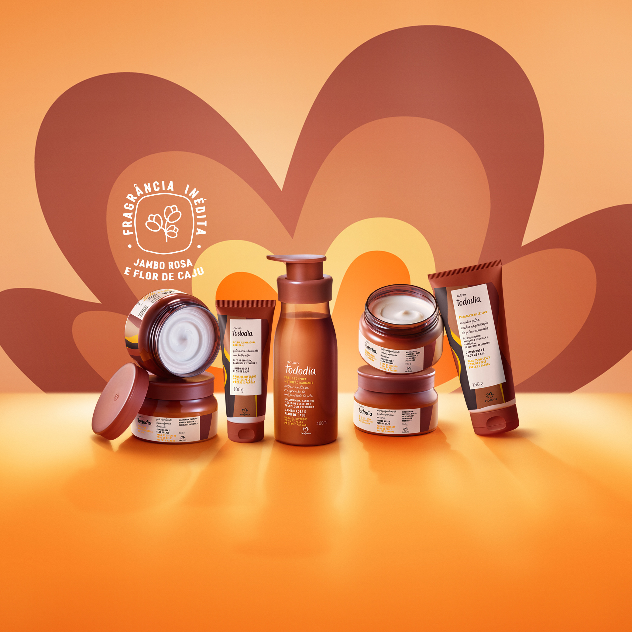 7 produtos Tododia na fragrância Jambo Rosa e Flor de Caju, em potes, bisnagas e frascos. Fundo em tons de laranja e marrom. 