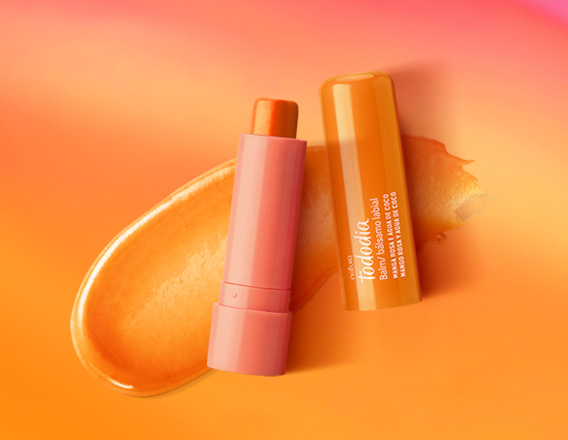 Embalagem laranja aberta de Balm Labial Tododia Manga Rosa e Água de Coco sobre textura cremosa laranja em fundo em tons de laranja e rosa.