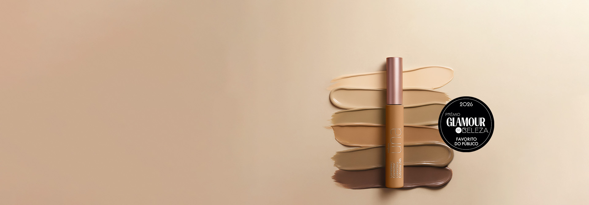 Corretivo Natura Una posicionado verticalmente no centro. Atrás dele, seis pinceladas horizontais de diferentes tons de base e corretivo estão dispostas em degradê, indo do bege claríssimo no topo ao marrom escuro na base, sobre um fundo neutro. Selo circular preto do "Prêmio Glamour de Beleza 2026", com a frase "favorito do público" na parte inferior.
