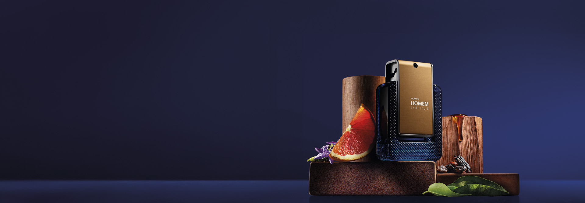Fragrância Natura Homem Evolut.io sobre madeiras e ingredientes como folhas e cítricos, em fundo azul escuro.