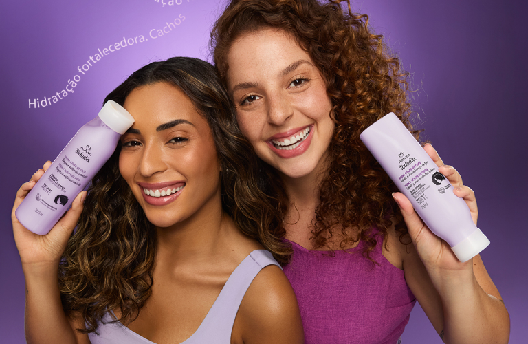 2 mulheres com cabelos cacheados segurando produtos da linha Tododia Cabelos Amora e Óleo de Coco