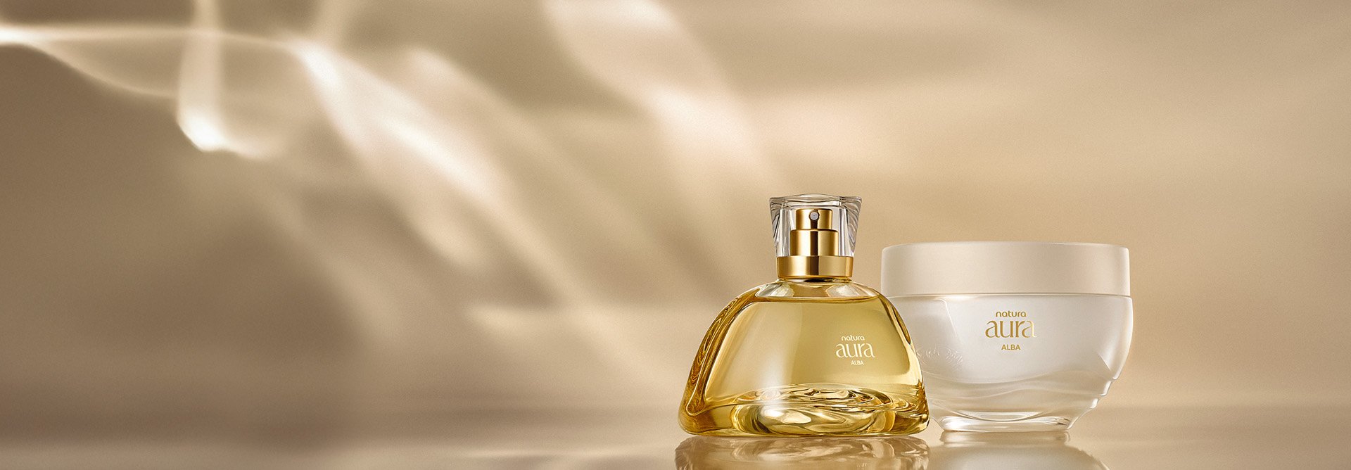 Presente Natura Aura Alba Completo, contendo 1 deo parfum com frasco de vidro e tampa transparente e 1 creme aveludado corporal, com frasco de vidro e tampa bege. Fundo bege-claro com reflexos de luz.