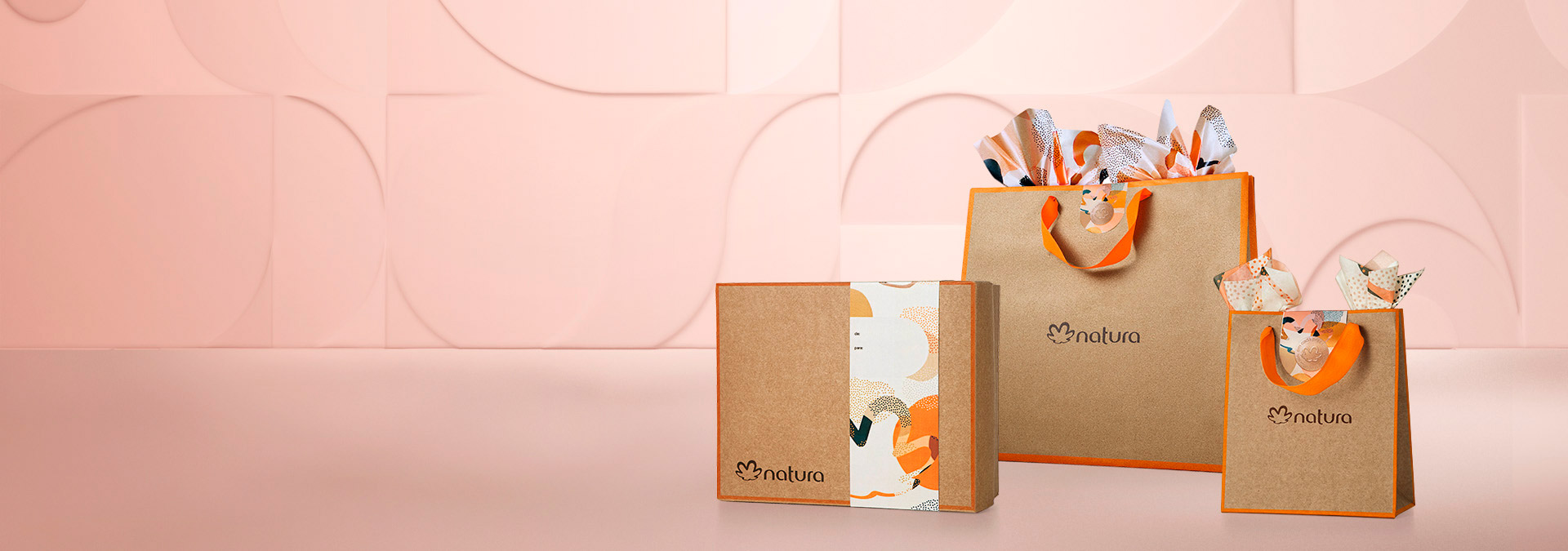 Fondo rosa y a la derecha dos bolsas y una caja de regalos marrones con detalles naranjas.