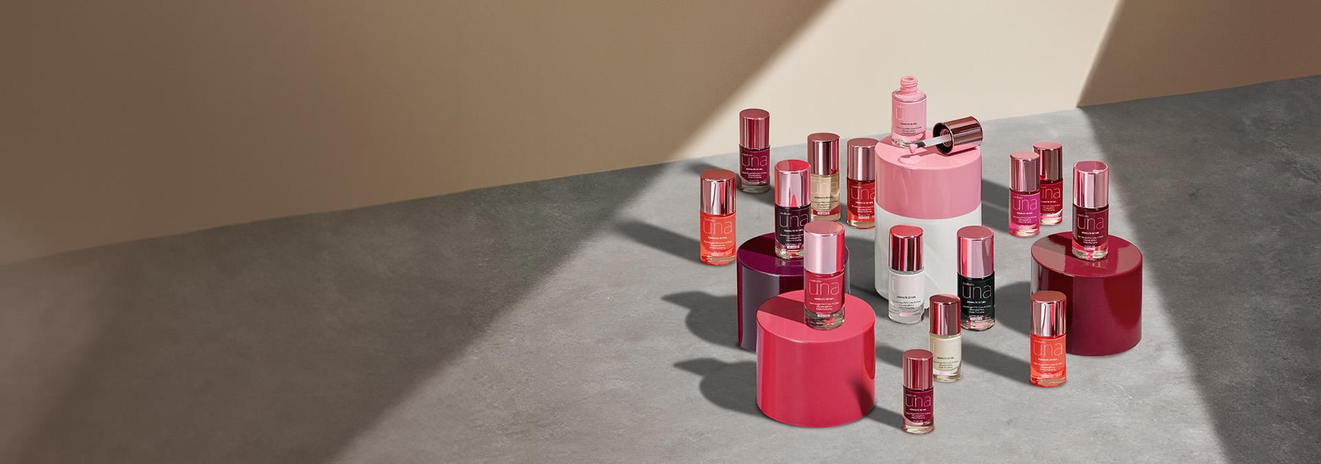 Esmaltes Natura Una en plataformas redondas de colores sobre una mesa gris, pared beige al fondo con rayos de luz