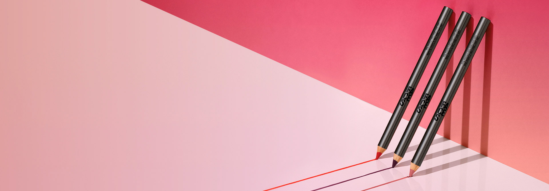 Imagen con fondo rosa claro y, en el lado derecho, tres lápices labiales Natura Una apoyados en la pared.