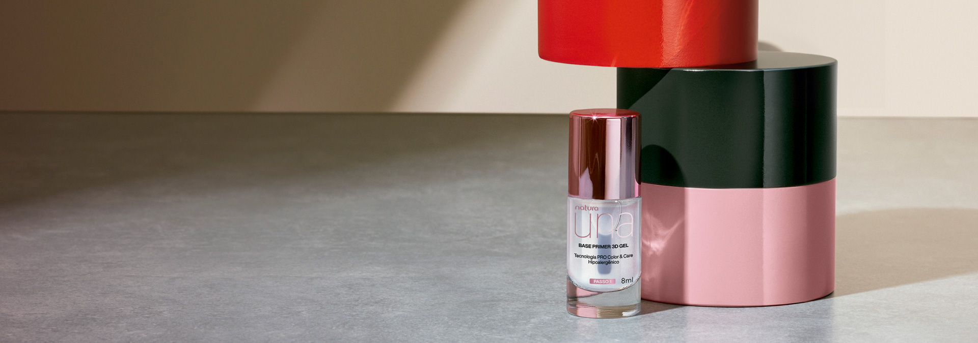 Fondo gris y a la derecha tenemos la base para uñas Una con elementos rosas, negros y rojos al fondo