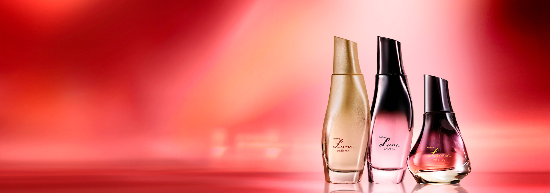Tres frascos de perfume Natura Luna, en tonos, uno al lado del otro, con fondo en tonos de rosa y rojo.