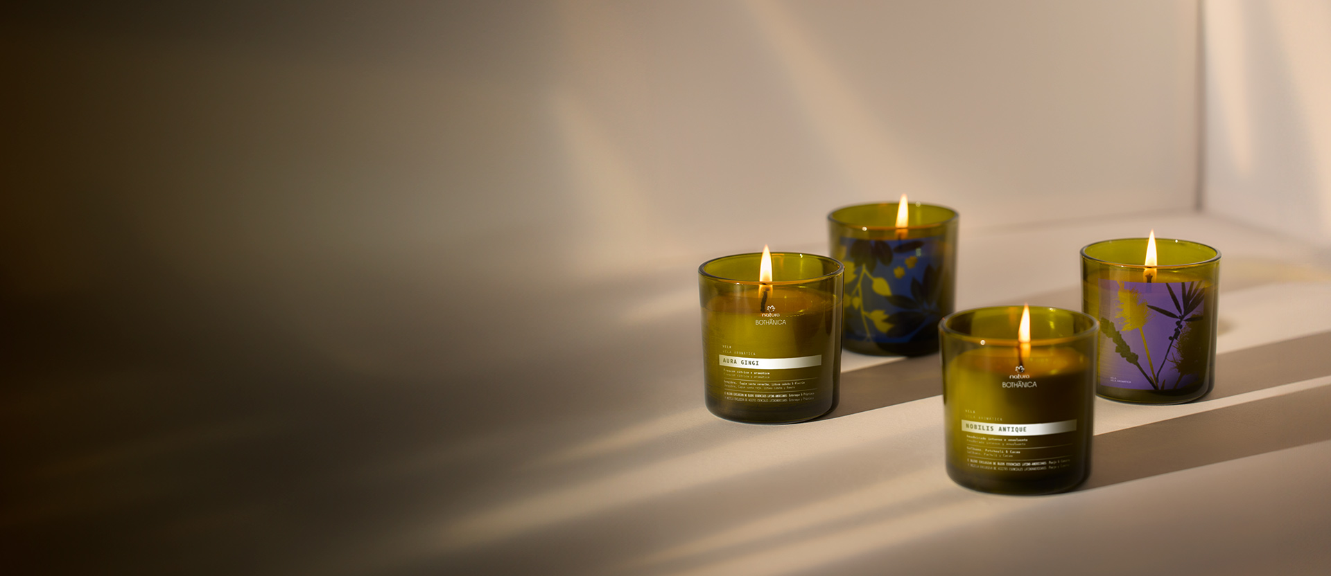 Cuatro velas perfumadas de Natura Bothanica en tonos verdes y morados, alineadas sobre una superficie clara con sombras suaves.