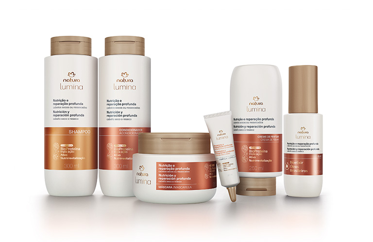 Foto de tres productos capilares de la línea Lumina sobre una superficie blanca con fondo azul. Incluye shampoo, acondicionador y mascarilla para el cuidado del cabello seco o dañado.