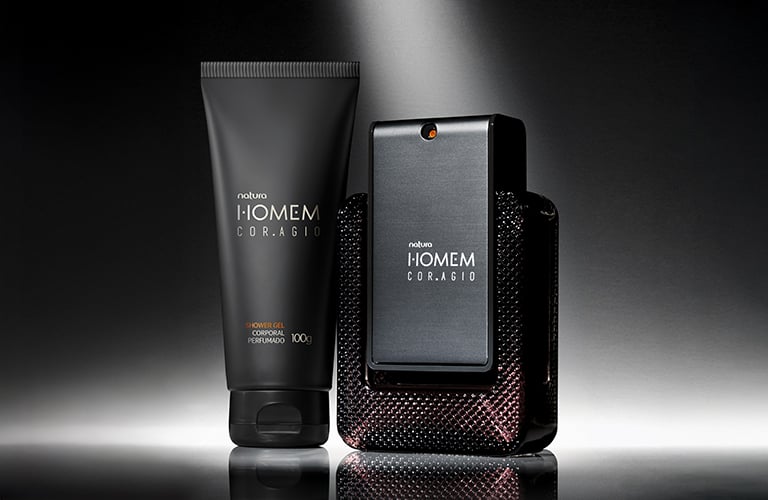 Sobre un fondo oscuro con un foco de luz, se aprecia un tubo de crema y un frasco de perfume de la línea Homem.