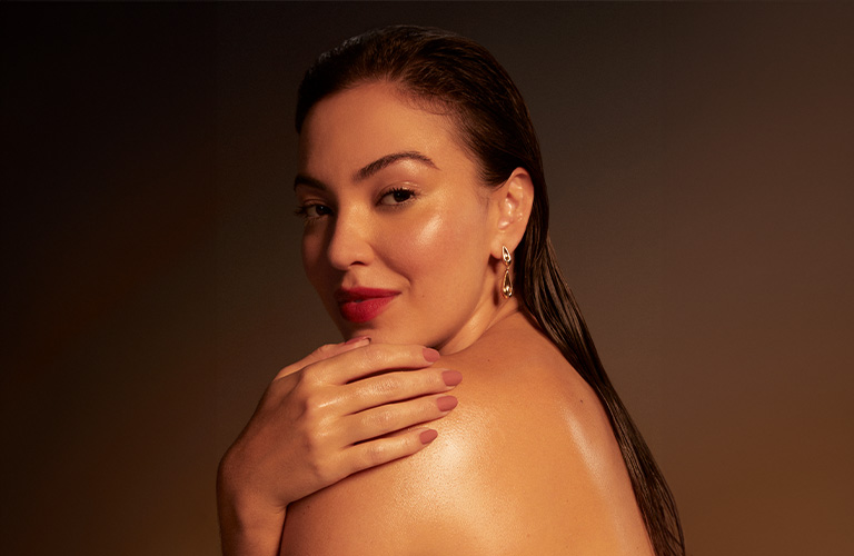 Modelo con el cabello mojado, sentada, mirando sobre el hombro mientras está de espaldas