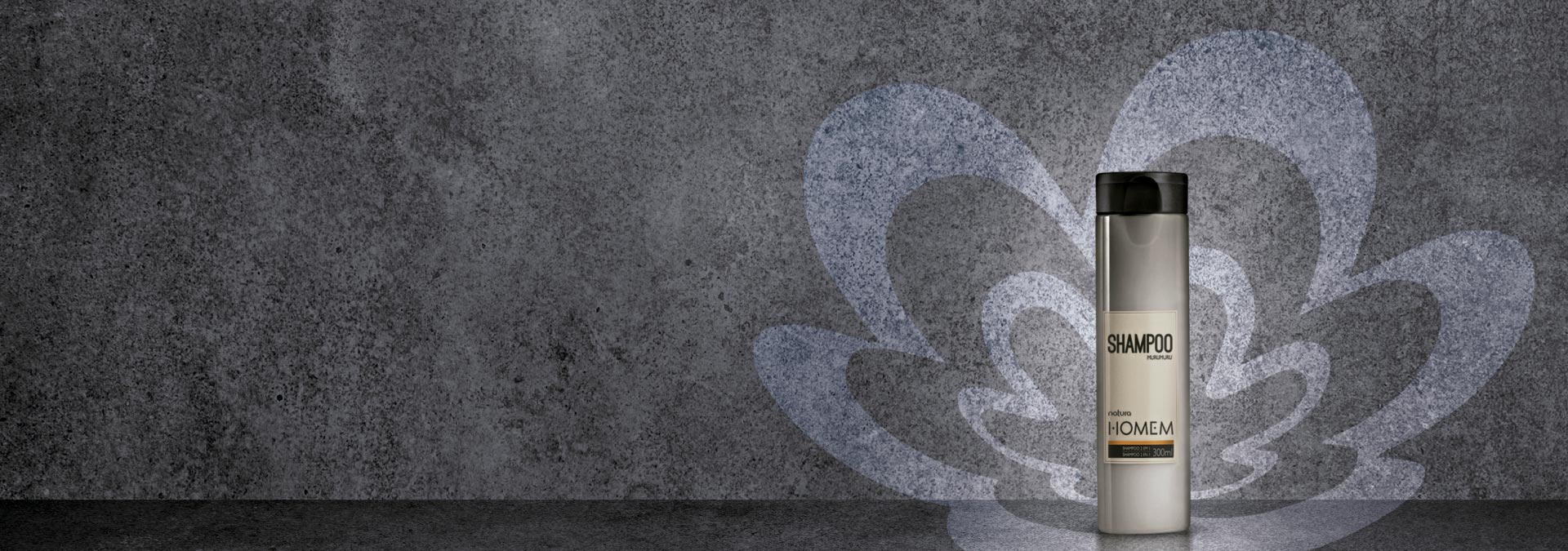 Fondo en tonos de gris oscuro y a la derecha el shampoo dos en uno Natura Hombre y rosáceo al fondo​