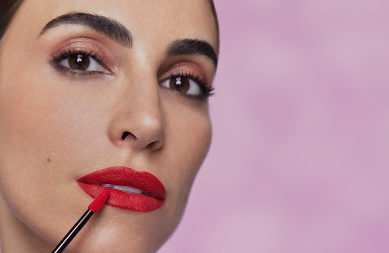 Close up del rostro de la modelo colocándose labial rojo.