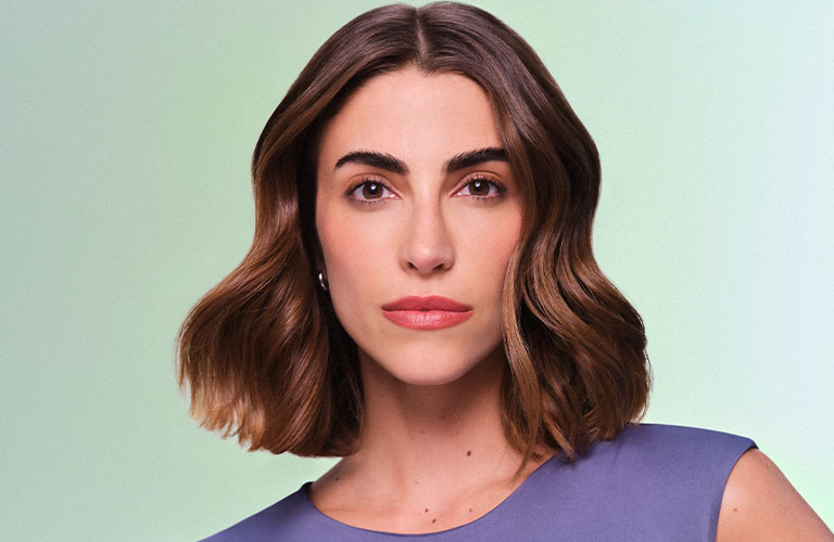 Close up de modelo con el cabello suelto, usando maquillaje Natura y con una blusa morada.