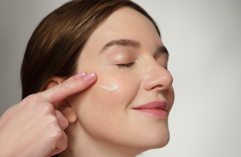 Close up modelo colocándose sérum en su mejilla con los dedos.