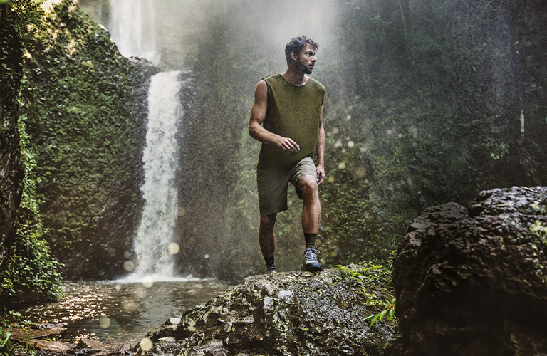 Hombre haciendo trekking en un ambiente natural con una cascada de fondo.