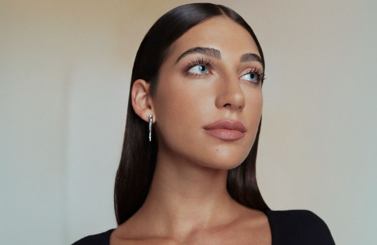 Close up de modelo con el cabello peinado detrás de las orejas, utilizando maquillaje Natura y una blusa negra.