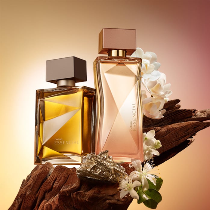 Imagen con fondo de gradientes entre amarillos y beige, trayendo al frente 2 de nuestras fragancias Essencial sobre un tronco de madera y rodeadas de sus flores aromáticas