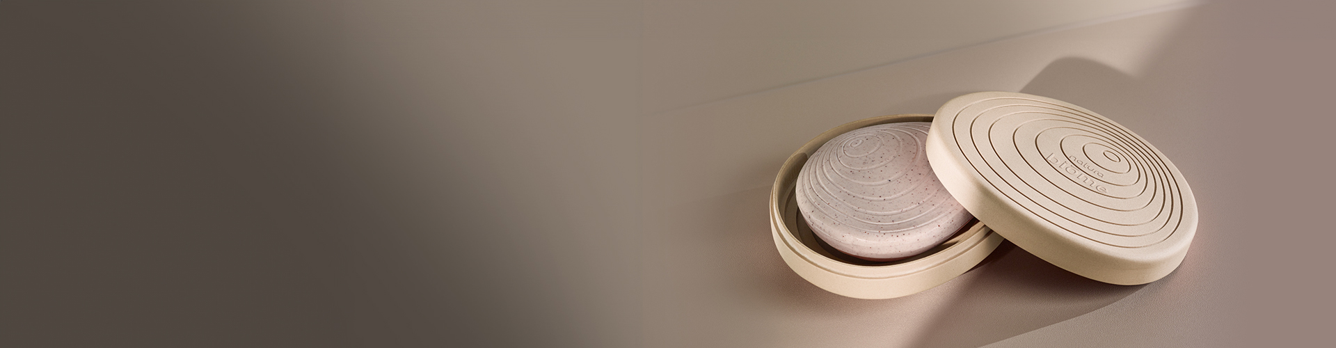 Imagen con fondo claro muestra un recipiente semiabierto, revelando un producto de la línea Natura Biome.