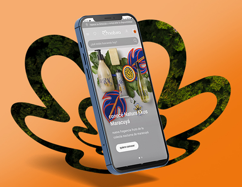 Banner con fondo naranja y elementos en verde. Presenta un celular mostrando productos de Natura. El texto invita a descargar la app para elegir y comprar con descuentos. 
