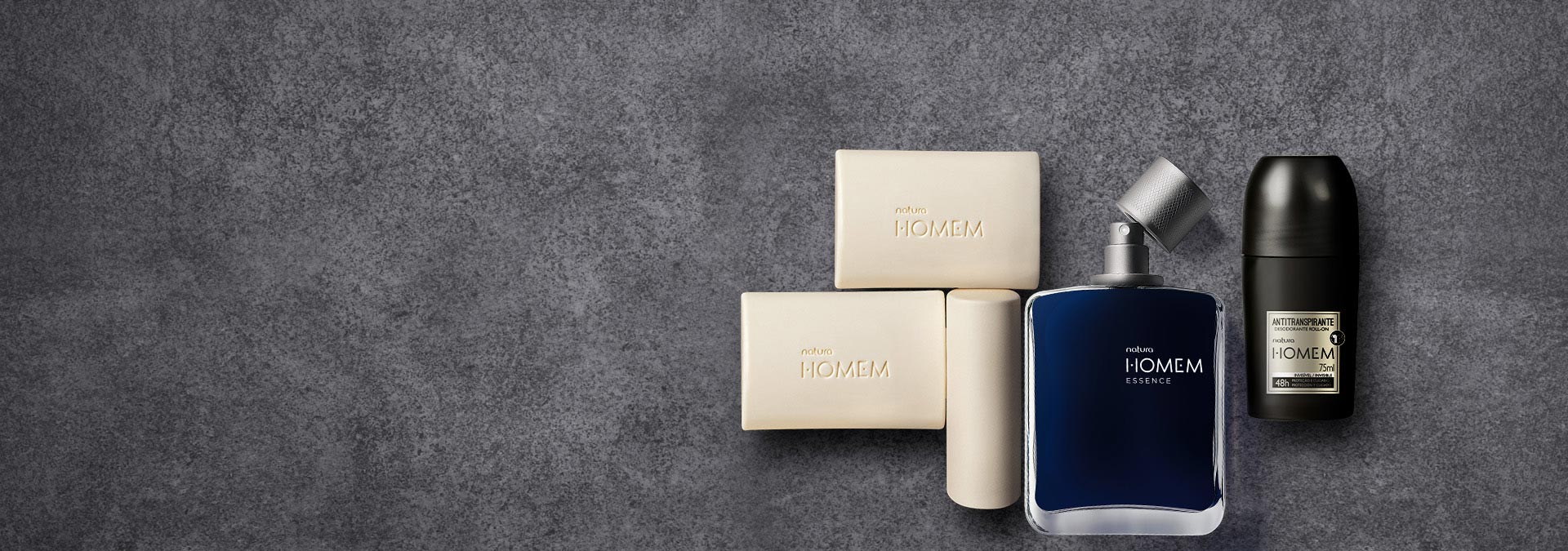 Fundo cinza escuro com 3 produtos da linha Natura Homem destacados, sabonetes em barra, perfume Essence e desodorante.